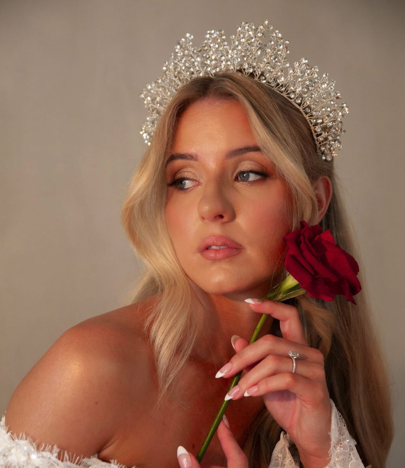 A bride in a crystal crown holding a red rose